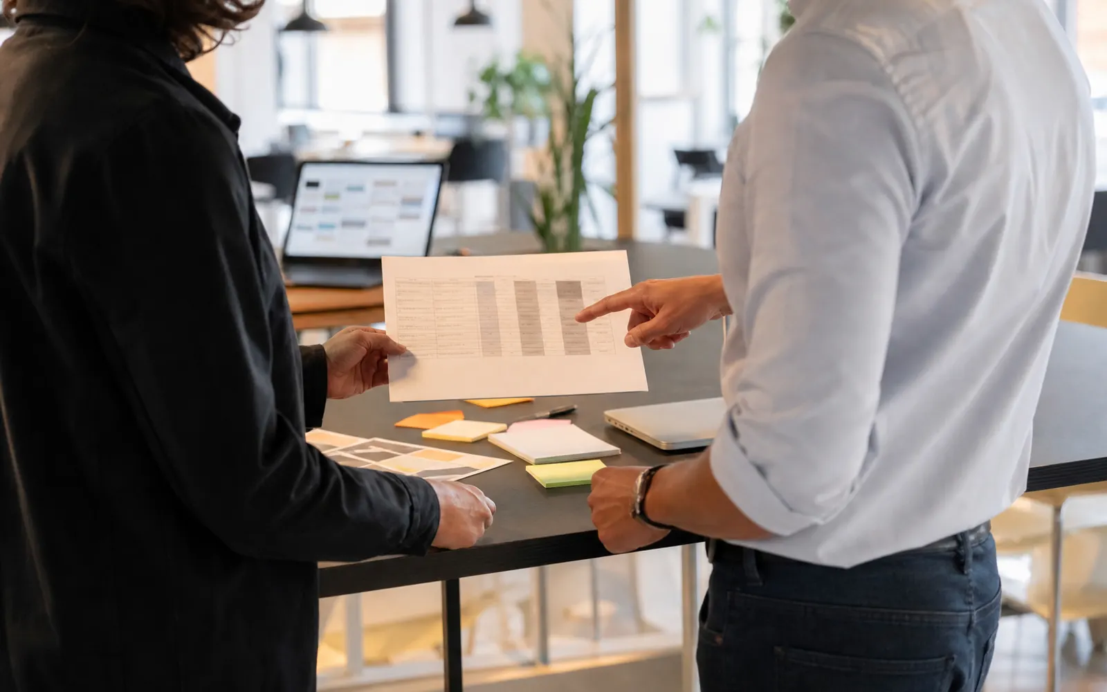 Deux collègues de dos devant une table haute, examinant un document comparatif imprimé
