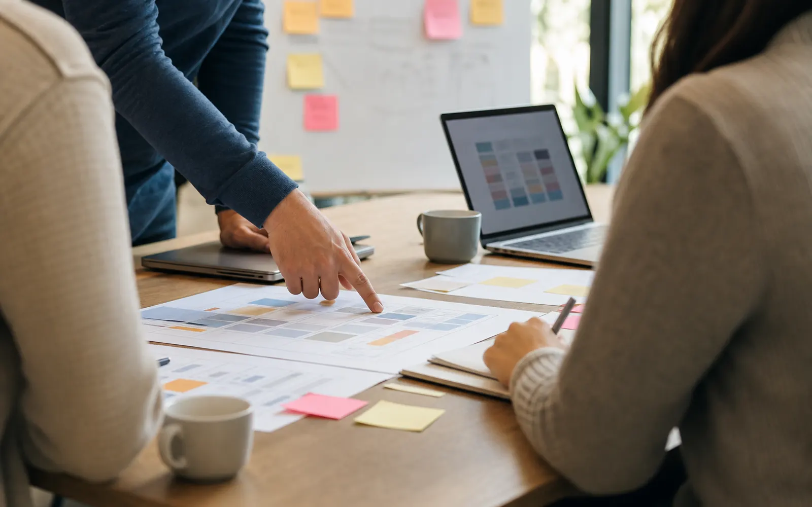 Trois personnes en réunion d'arbitrage autour d'une table couverte de feuilles de comparaison imprimées