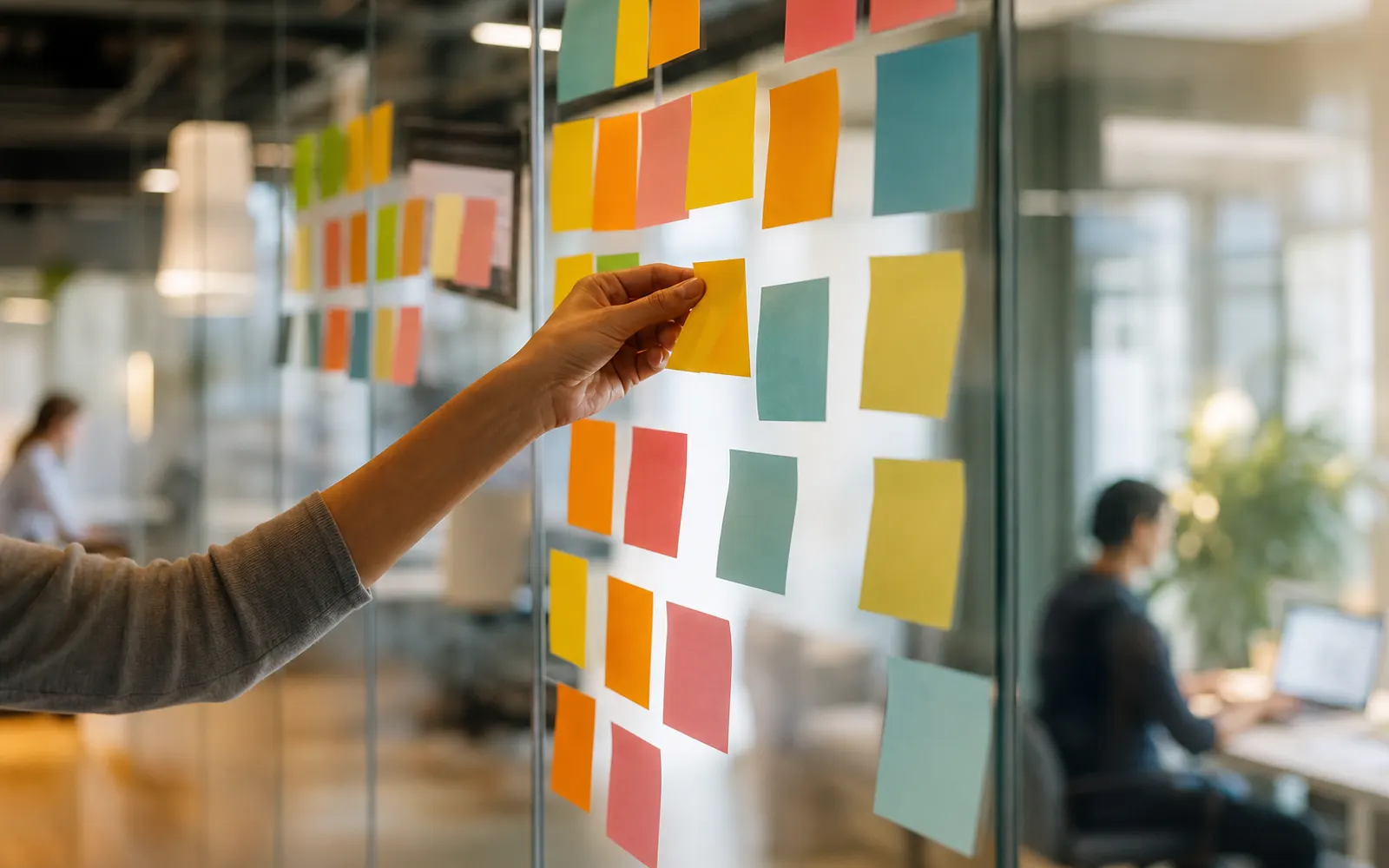 Mur de post-it colorés organisés en colonnes, une main déplaçant une note